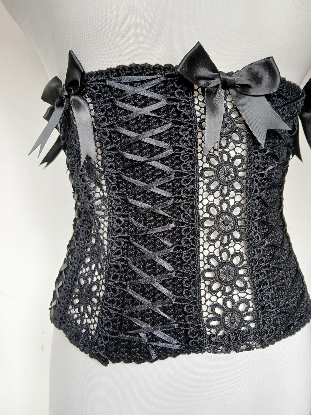 Gothic Lace Corset Belt The Dark Duchess — close up detail of black handmade crochet corset with guipure lace panel, satin ribbon criss-cross lacing and black satin bows on white mannequin - Victorian Velvet