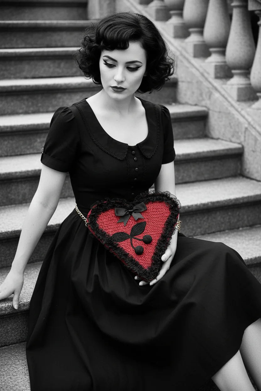 Black and white color pop editorial — pin-up model in black dress sitting with the red Poison Cherry Heart Bag on her lap - Victorian Velvet