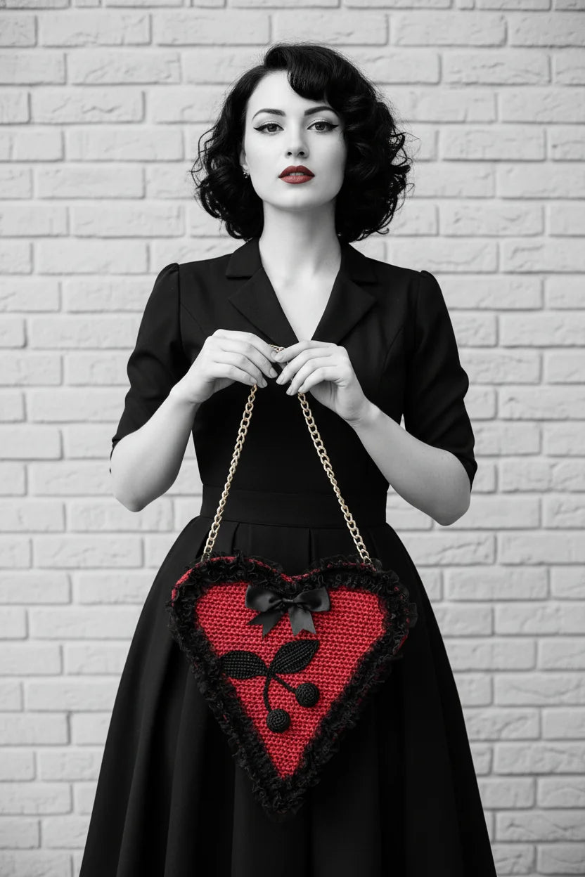 Black and white color pop editorial photo — pin-up model in black dress holding the red Poison Cherry Heart Bag with both hands against a white brick wall - Victorian Velvet