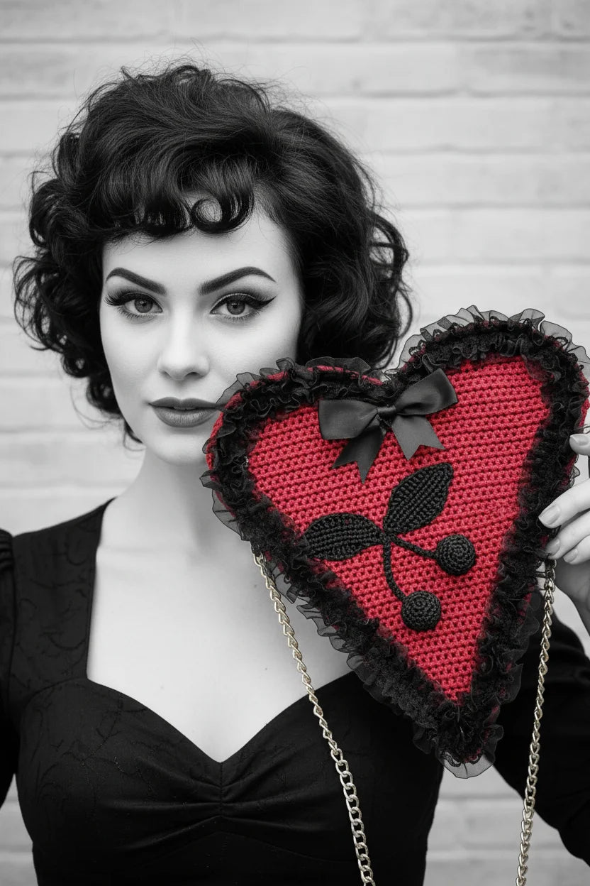 Black and white color pop close-up portrait — pin-up model with black hair and red lips holding the red Poison Cherry Heart Bag next to her face, light brick wall background - Victorian Velvet