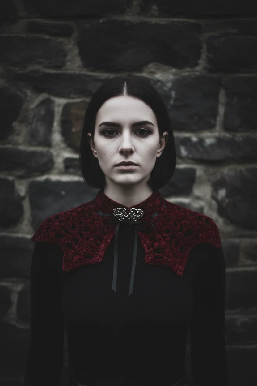 Pale gothic woman with short dark hair wearing a deep burgundy velour crochet bat wing collar with silver baroque brooch and black satin ribbon, standing against dark stone ruins, gothic fashion editorial - Victorian Velvet