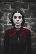 Pale gothic woman with short dark bob hair wearing a deep burgundy velour crochet bat wing collar with silver baroque brooch and black satin ribbon, standing against grey stone wall, gothic fashion editorial - Victorian Velvet