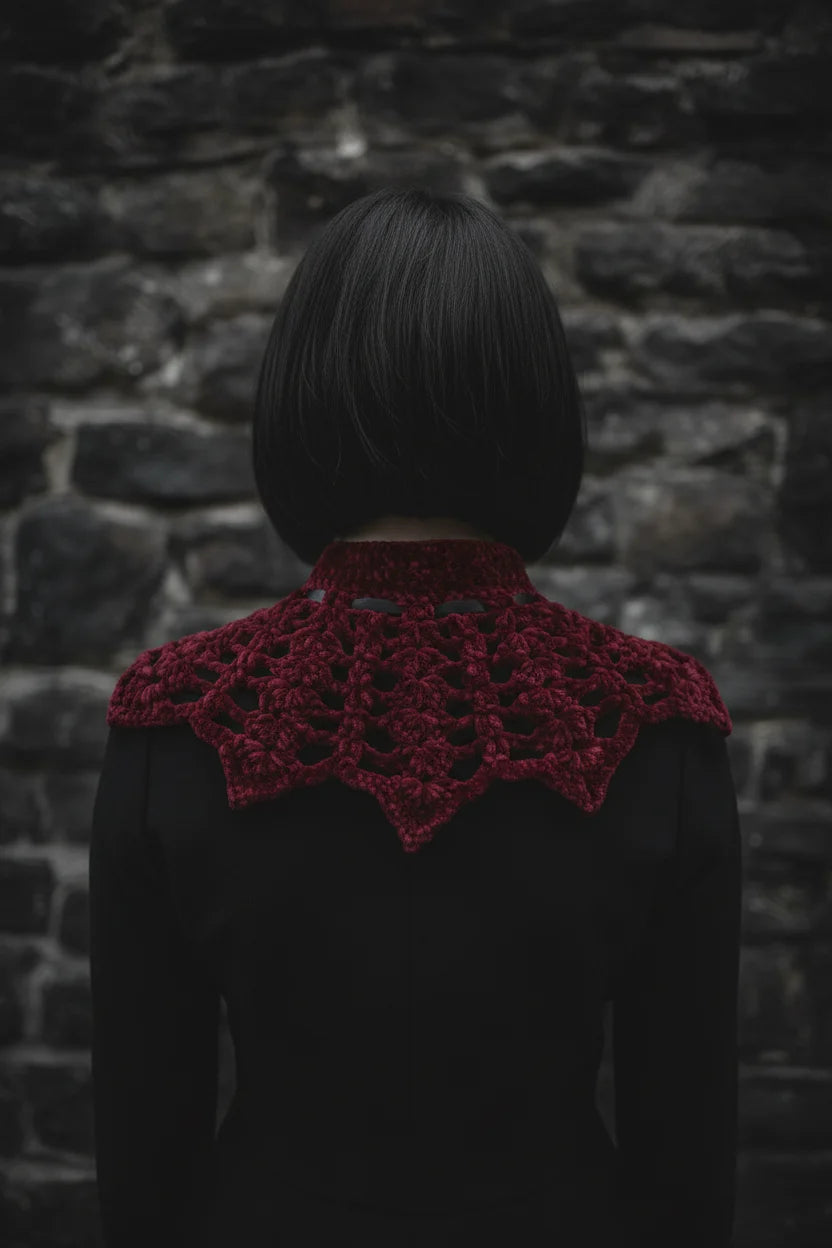 Back view of a pale gothic woman wearing a deep burgundy velour crochet bat wing collar with open lace spider web pattern draping over shoulders and upper back, dark stone wall background - Victorian Velvet