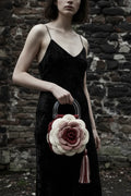 Woman in black velvet slip dress holding a cream and burgundy crochet rose handbag with clear acrylic handle and striped tassel, standing against a rough dark stone wall, gothic fashion editorial - Victorian Velvet