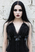 Cathedral Lace Corset – pale gothic model with long dark hair wearing black handmade crochet halter corset with lace ruffles and satin bows, front view, white stone wall background - Victorian Velvet