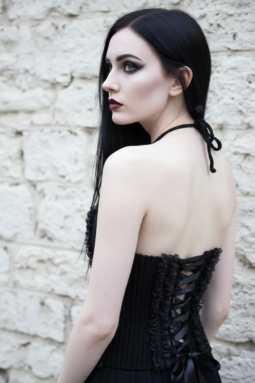 Cathedral Lace Corset – pale gothic model with long dark hair, back view showing satin lace-up closure and black lace ruffles, face turned over shoulder, white stone wall background - Victorian Velvet