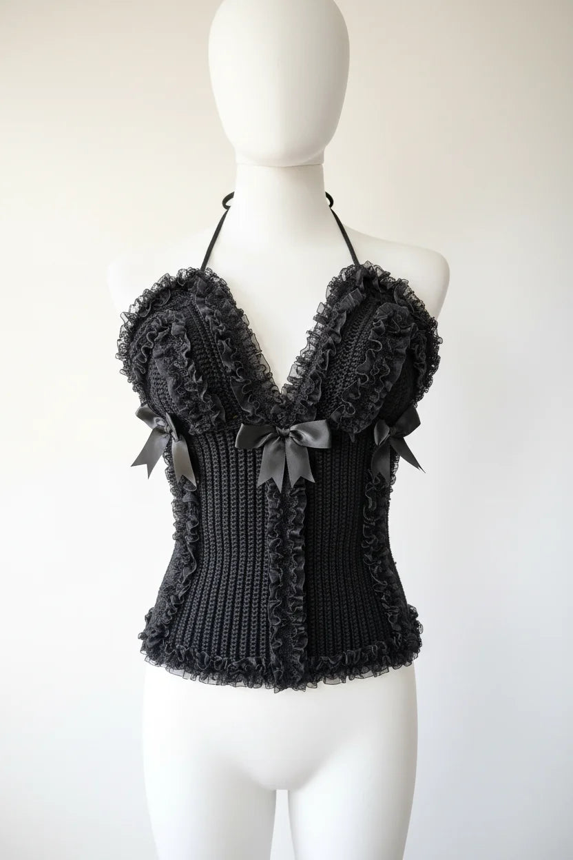 Front view of a black crochet halter corset top with deep V-neckline, black lace ruffles and three satin bows, displayed on a white dress form against a white background - Victorian Velvet