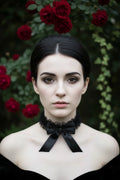 Gothic woman with dark hair in elegant updo wearing black organza ruffle choker with satin bow, front view, red roses and ivy garden background, Victorian Velvet handmade

