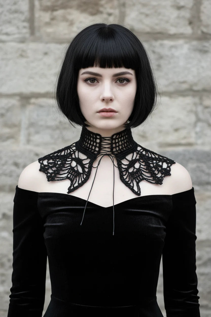 Front view of a pale gothic woman with short dark black bob hair with fringe wearing a black fine crochet lace collar with wide high turtleneck band with open square grid mesh pattern and black corset-style lace-up ribbon tie at center front, wide dramatic wing-shaped lace crochet panels draping over both shoulders with intricate gothic lace pattern and scalloped pointed tips, worn over a black off-shoulder velvet dress, grey stone wall background - Victorian Velvet