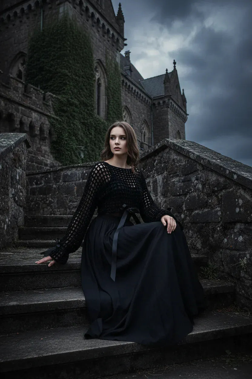 Elegant woman in black velvet crochet mesh sweater with satin ribbon bows sitting on ancient stone castle steps with ivy covered gothic walls and dramatic cloudy sky - Victorian Velvet
