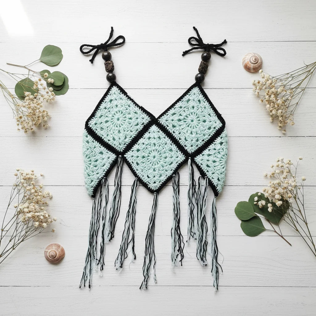 Mint green and black crochet granny square crop top with fringe and black beaded straps, flat lay on white wooden table with dried flowers and shells - Victorian Velvet