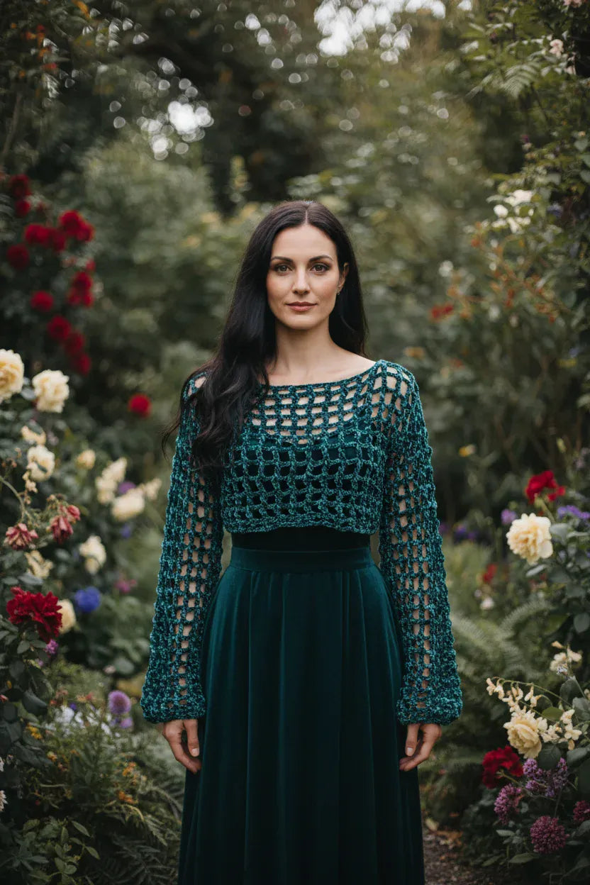 Woman wearing forest green velvet crochet mesh sweater with wide boat neckline standing in a blooming rose garden - Victorian Velvet
