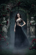Woman wearing black handmade crochet spiderweb top with sweetheart neckline standing in a gothic garden with stone statues, red roses and iron gate in the mist - Victorian Velvet
