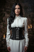 Gothic Lace Corset Belt The Dark Duchess — close up front view, model with long dark hair wearing black handmade crochet corset with guipure lace panel and satin bows, gothic stone wall with candles - Victorian Velvet