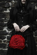 Woman in black Victorian lace dress holding a red crochet rose handbag with black handles against a rough dark stone wall, gothic fashion editorial - Victorian Velvet