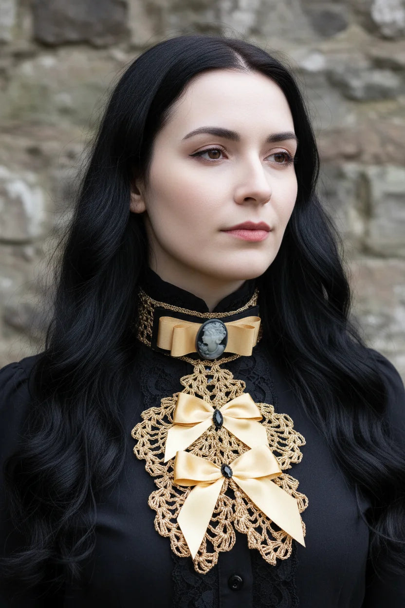 Handmade gold crochet jabot with gold satin bows and grey cameo brooch on black velvet choker, worn over a black Victorian blouse with stand-up collar, portrait against stone wall - Victorian Velvet