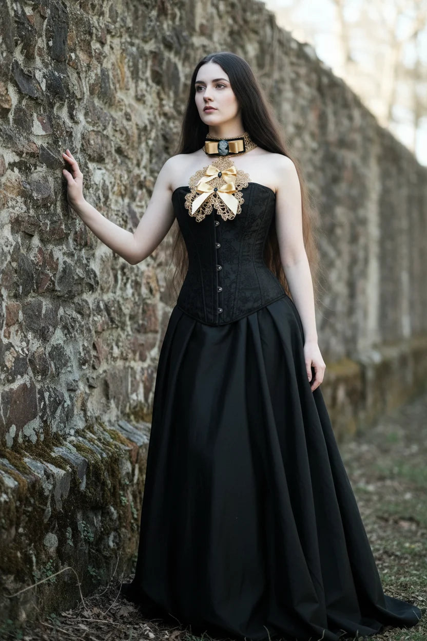 Handmade gold crochet jabot with gold satin bows and cameo brooch on black velvet choker, worn with black corset and long black skirt, full length portrait against stone wall - Victorian Velevt
