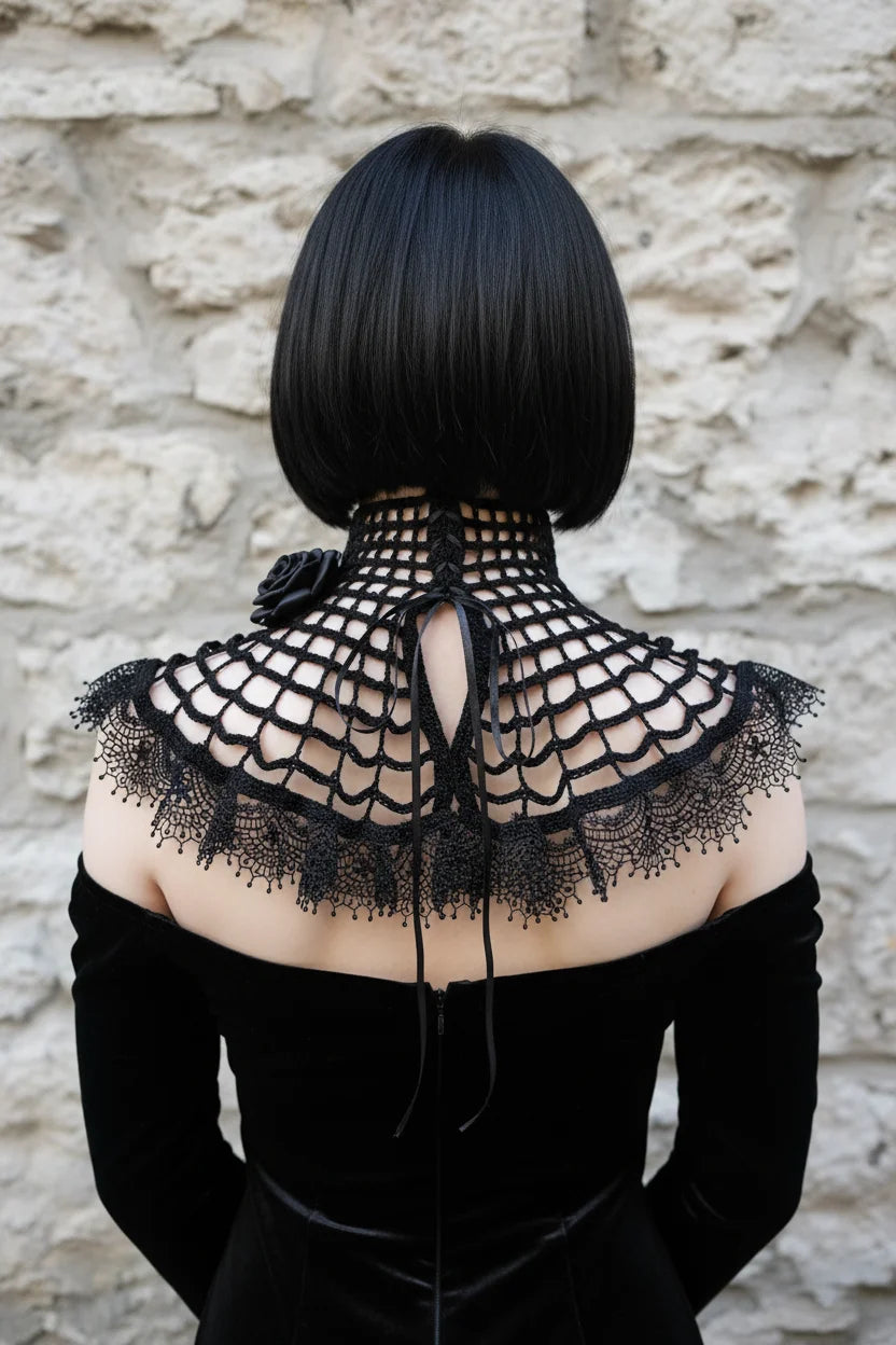 Back view of a pale gothic woman with short dark black bob hair wearing a black crochet spider web collar capelet over a black off-shoulder velvet dress with bare upper back, high fitted open grid mesh turtleneck band with black satin ribbon lace-up closure and long ribbon ties hanging down at center back, wide circular capelet with spider web crochet pattern spreading symmetrically over both shoulders, wide black lace ruffle trim with bead drops at the outer edge, one black satin rose at the left shoulder 
