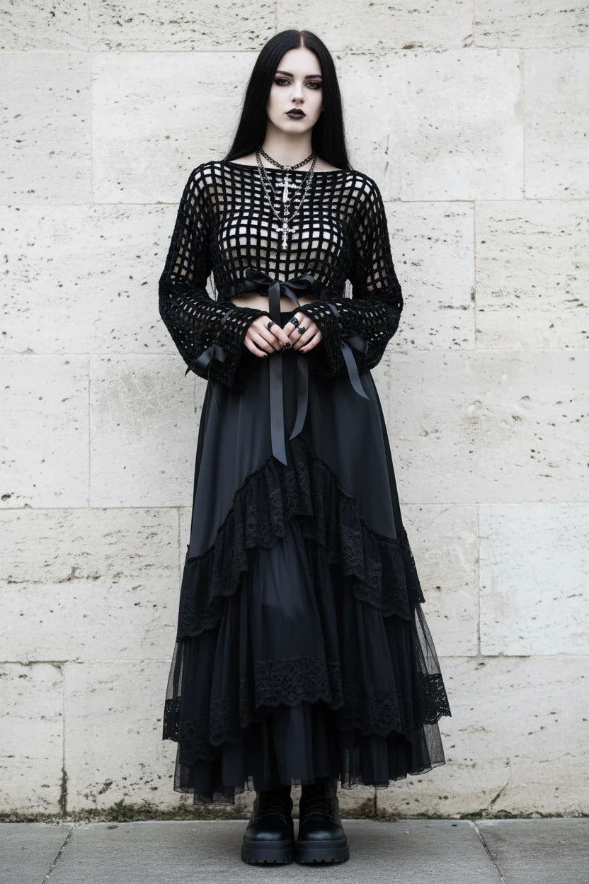 Black velour grid crochet crop top with long sleeves and satin bow ties at waist, worn with long black tulle skirt, gothic model with dark makeup and cross necklace, stone wall background - Victorian Velvet