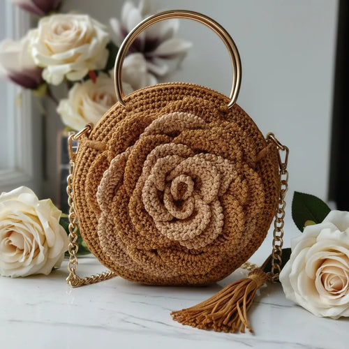 Handmade golden crochet rose handbag with gold ring handle, gold chain strap and golden tassel, displayed on white marble surface with cream roses, close-up showing detailed crochet texture by Victorian Velvet